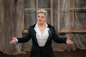 Eddie Izzard stands on a stage looking out to the audience 