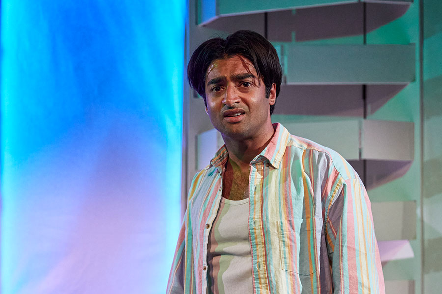 Nikhil Parmar stands on stage in a white unbuttoned shirt, looking incredulously at the camera