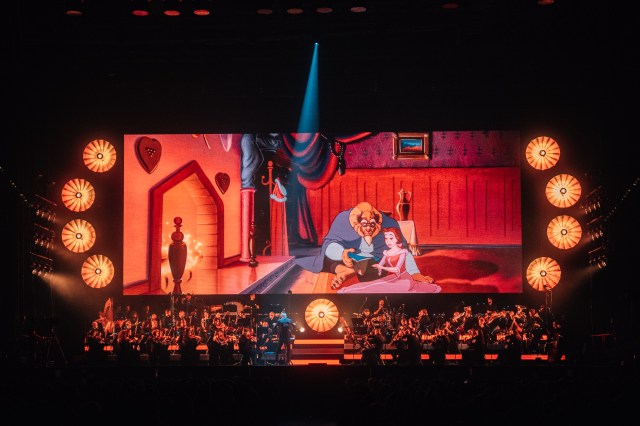 A scene from Disney's <em>Beauty and the Beast</em> plays on a giant screen above the orchestra during <em>Disney100: The Concert</em>