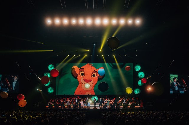 A scene from Disney's <em>The Lion King</em> plays on a giant screen above the orchestra at <em>Disney100: The Concert</em>