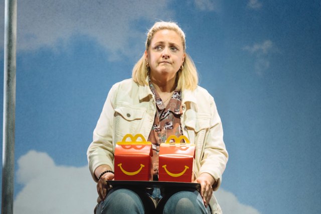 Laura Checkley as Hope, sat on stage and holding a Happy Meal box