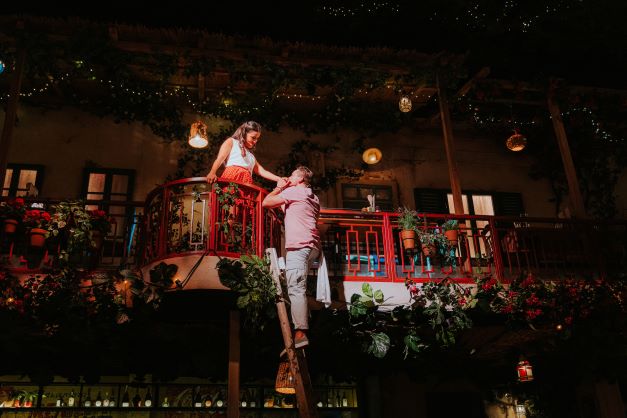 Noah Sinigaglia at a balcony and Luke Friend on a ladder next to her in a scene from <em>Mamma Mia! The Party</em>