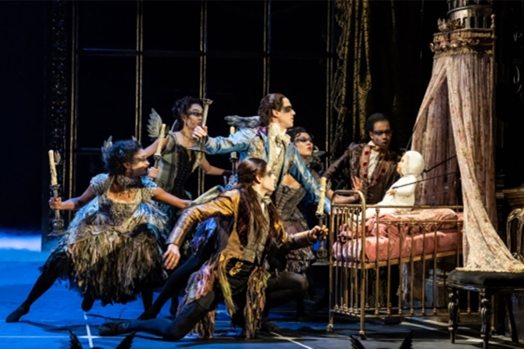 A scene from Matthew Bourne's Sleeping Beauty showing fairies gathering around a baby in a cradle