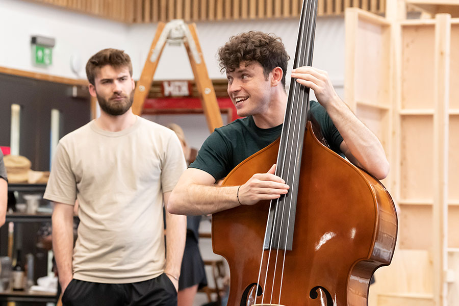 Charlie Stemp in rehearsals for Crazy for You, holding a double bass while speaking to an unseen figure out of frame