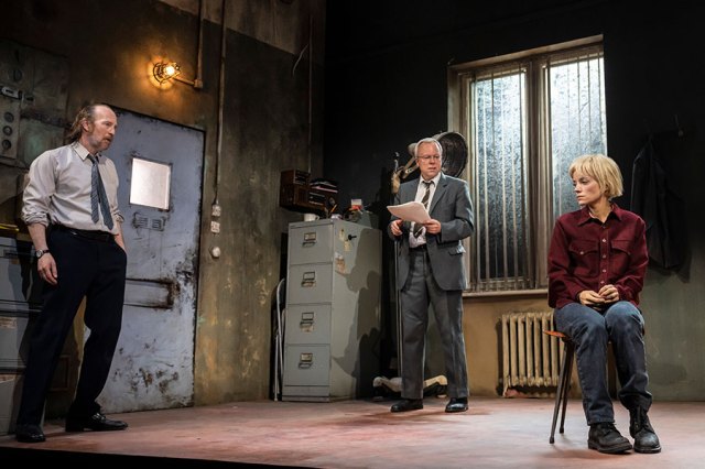 Three actors stand in an interrogation room set