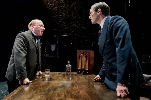 Adrian Scarborough and Stephen Campbell-Moore stand around a table in period costumes