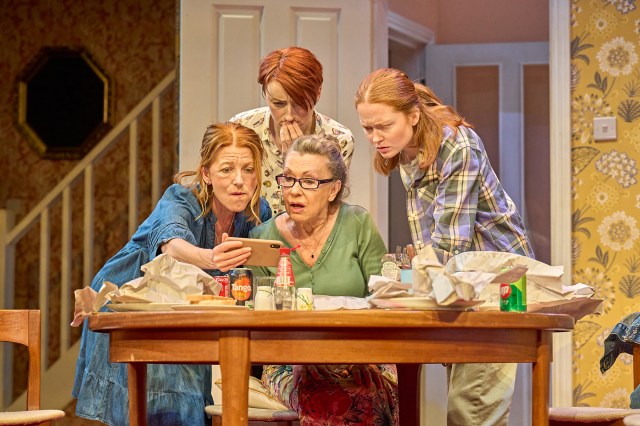 Four women gather around a dining room table looking at an envelope