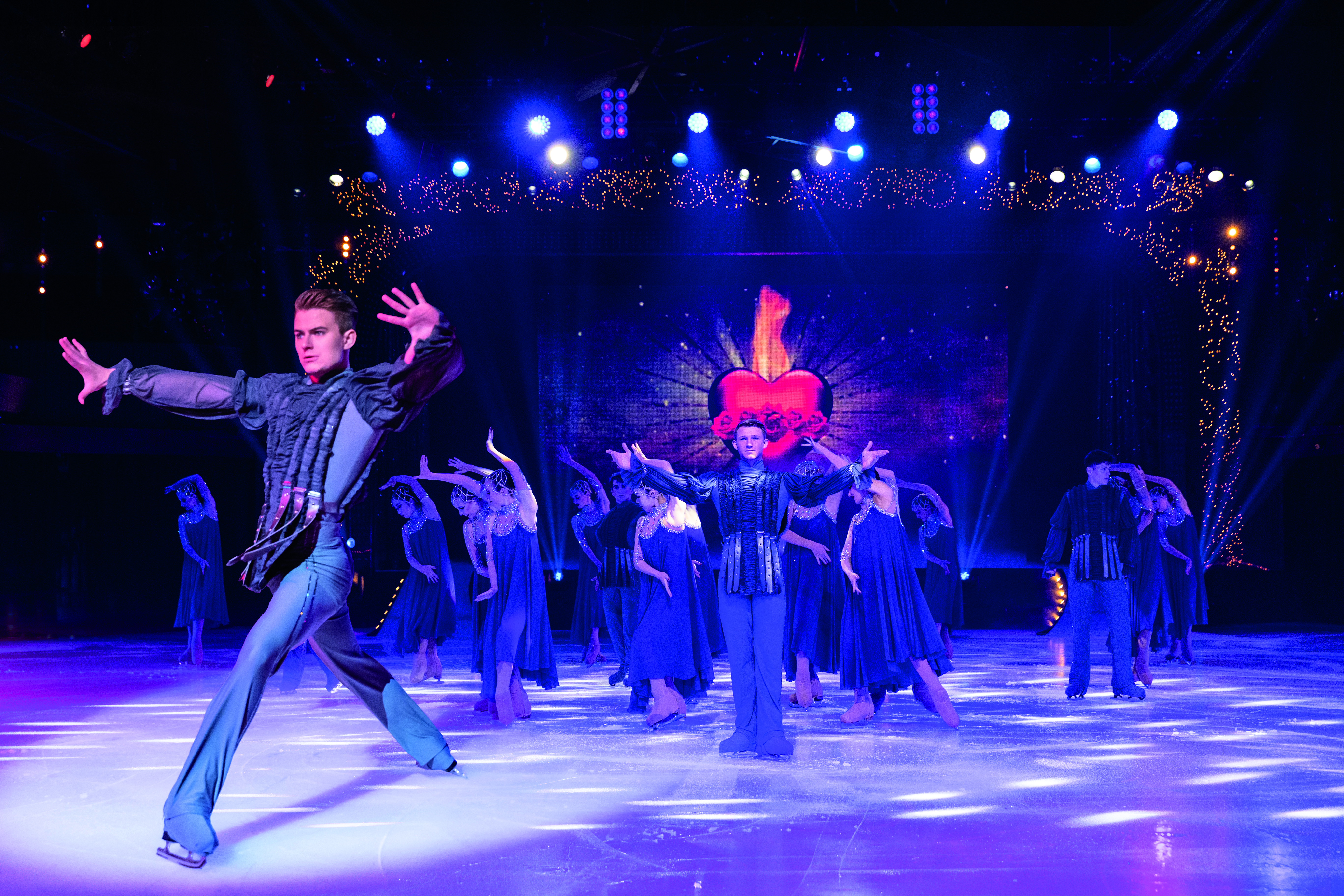 Ice skaters in elaborate, dark costumes pose on the rink in Blackpool