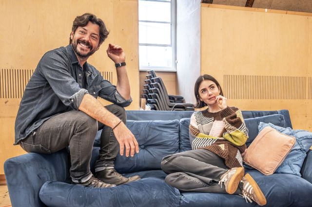 Álvaro Morte and Lily Collins sit on a navy sofa