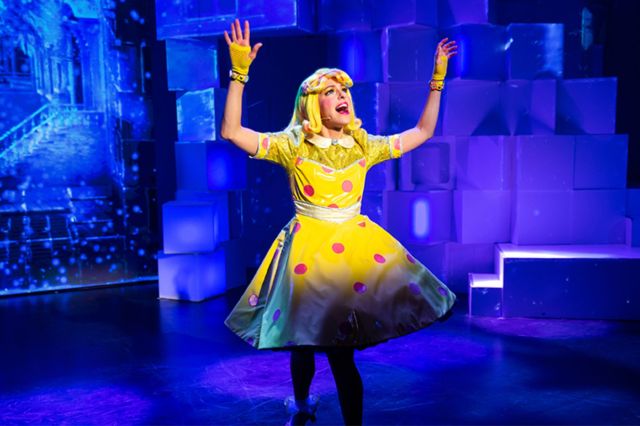 A performer wearing a yellow dress throws hands up