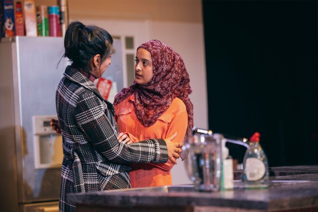 Two actresses embrace on a kitchen set