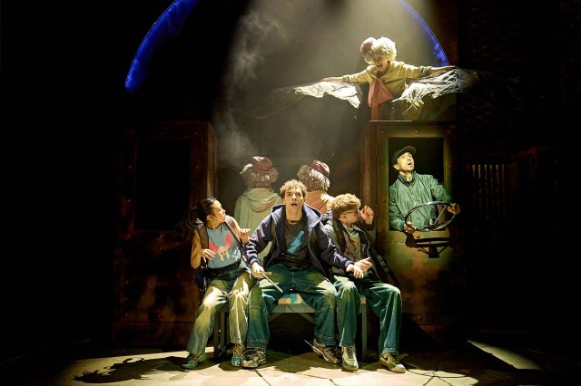 A group of actors pretending to sit on a bus with a harpy on the roof