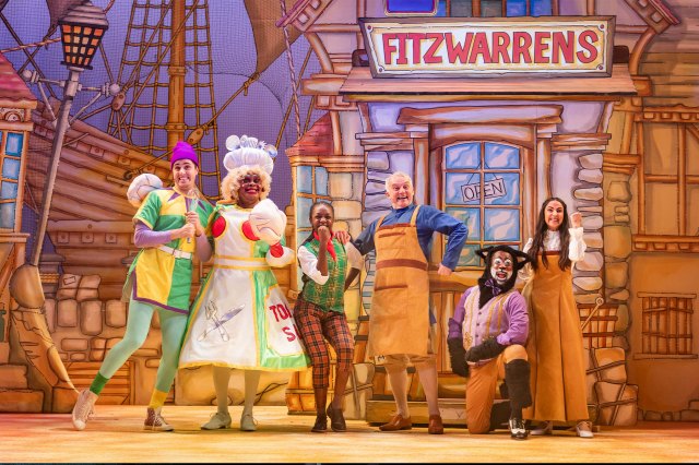 A line-up of actors in bright pantomime costumes on stage