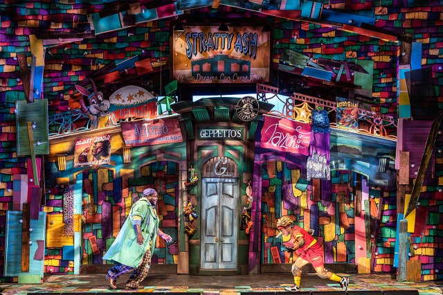 Pinocchio 2 Two actors, dressed as Geppetto and Pinocchio, on stage in front of a multi-coloured pantomime set