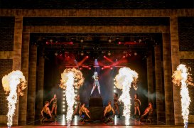 A scene from The Bodyguard musical with a pop singer surrounded by background dancers and flames