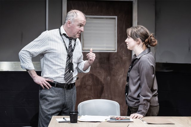 An actor and an actress portray two colleagues in an office setting on stage