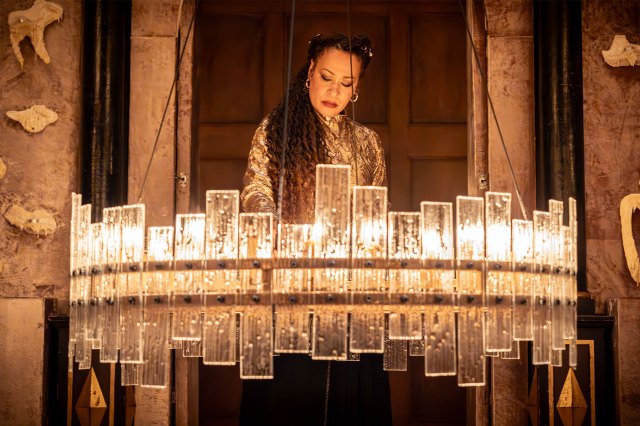 An actress on stage behind a glass fixture that holds many candles