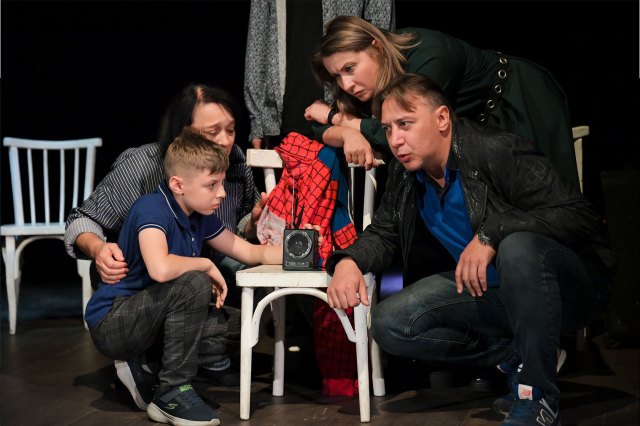 Four actors onstage portraying a family gathered around a radio, listening intently