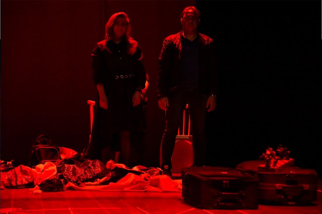Two silhouetted actors onstage under a dim red light