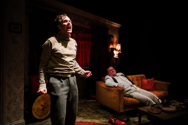 Two actors on stage in a dimly lit living room set
