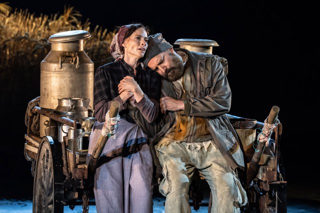 An actress and an actor in period costumes, sat on a milk cart