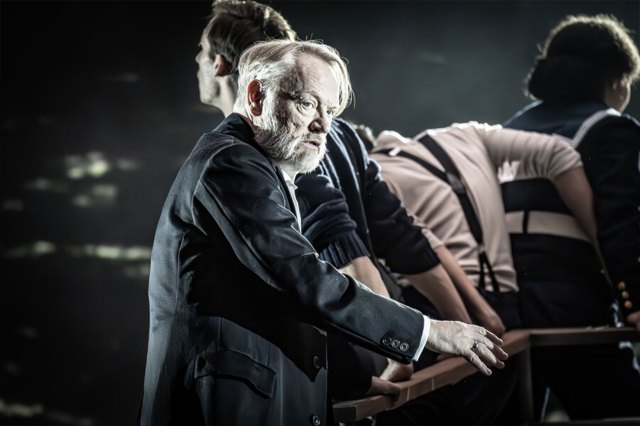 An older actor on stage, wearing a black jacket