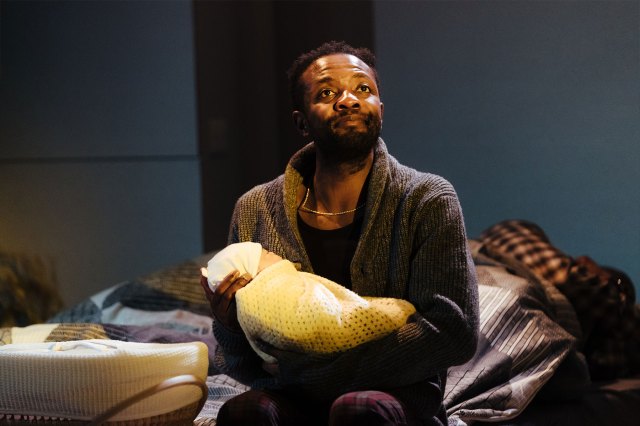 An actor on stage in a dressing gown, holding a baby