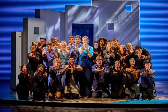 A group of actors on stage in front of a Greek building set