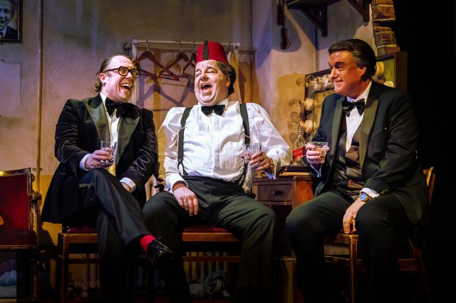 Three actors say side by side on stage, dressed as comedians Eric Morecambe, Tommy Cooper and Bob Monkhouse