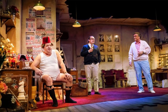 Three actors on stage on a backstage dressing room set, dressed as comedians Tommy Cooper Eric Morecambe and Bob Monkhouse