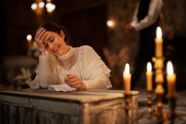 An actress in period dress sits at a candle-lit desk