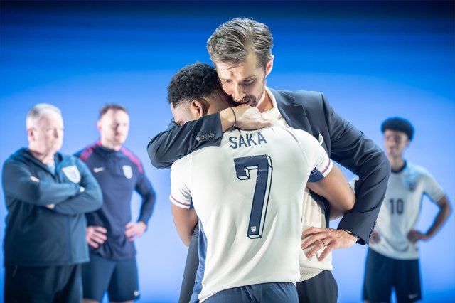 An actor dressed as Gareth Southgate consoles another actor dressed as footballer Bukayo Saka on stage
