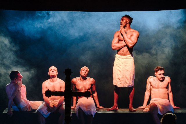 Five actors on stage wearing towels around their waists during a sauna scene
