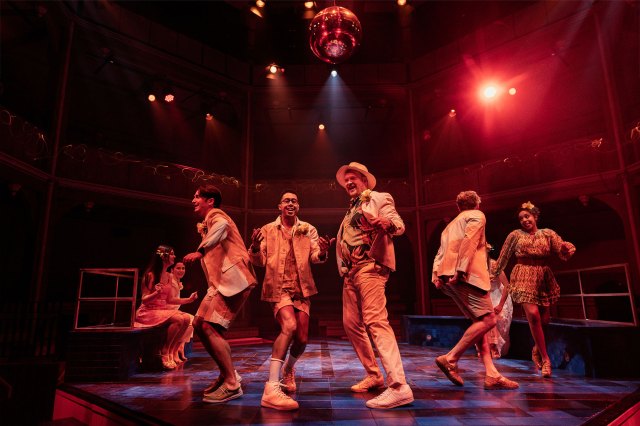 A group of actors on stage under a disco ball during a nightclub scene