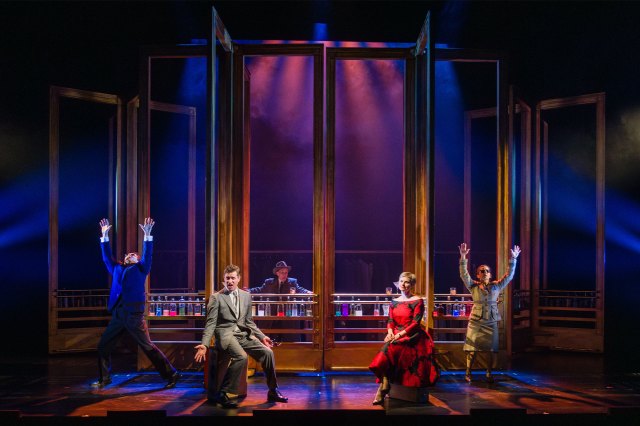 A group of actors on stage in a spy thriller-esque setting