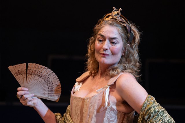 An actress on stage in 17th-century period dress, fanning herself