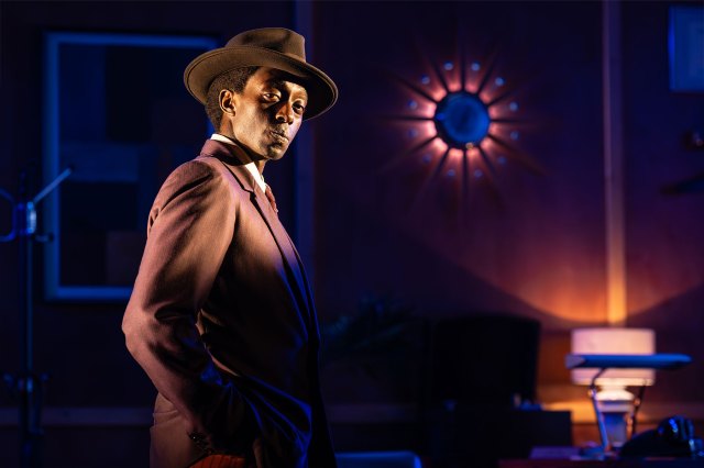 An actor dressed as Sidney Poitier on a dimly lit stage