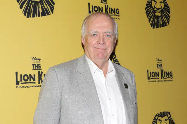 Lyricist Tim Rice in front of a yellow backdrop that displays The Lion King branding