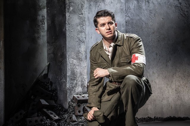 An actor, wearing a 1940's military medical uniform, crouches down on stage