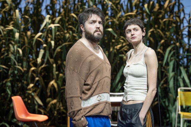 Two actors stand on stage in front of a leafy backdrop