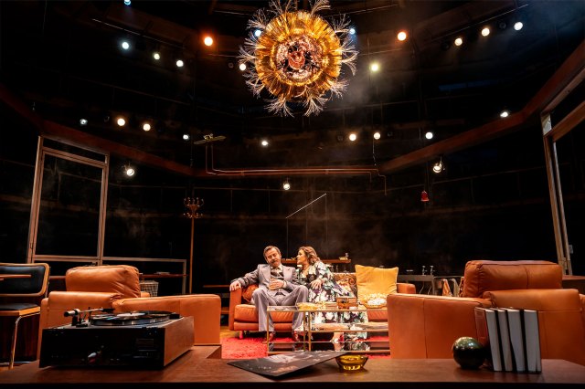 An actor and an actress sitting on a living room set on stage
