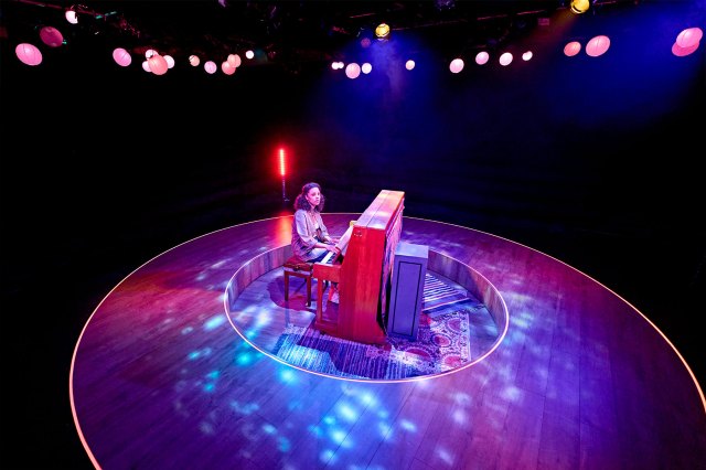An actress sat at a piano centre stage