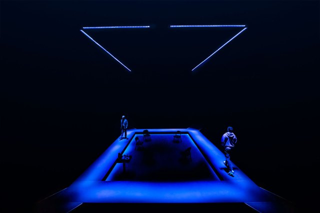 Two actors walking around a stage designed to resemble a blue-lit frame.