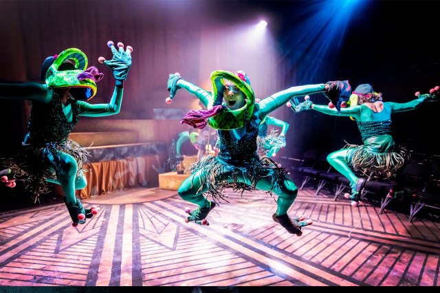 Four actors on stage, dressed as frogs leaping in the air