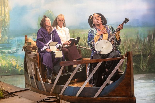 Three actresses sitting in a small wooden rowing boat on stage