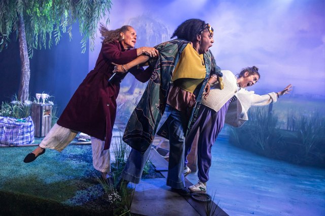 Three actresses teeter over a fake river on stage