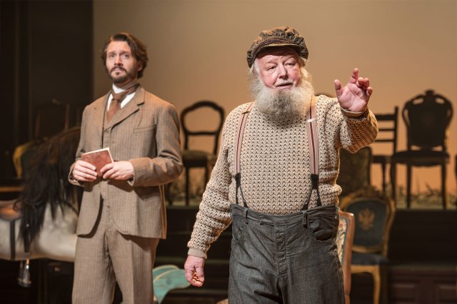 A smartly dressed actor in a late 19th-century-style suit and an older actor in common late 19th-century clothing.
