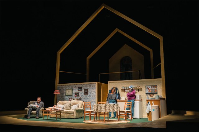 Three actors standing on an onstage living room set.