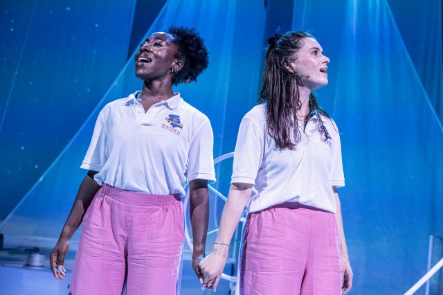 Two actresses in sailing costumes hold hands on stage.