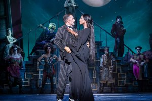 Two actors embrace on stage, dressed as Gomez Addams and Morticia Addams